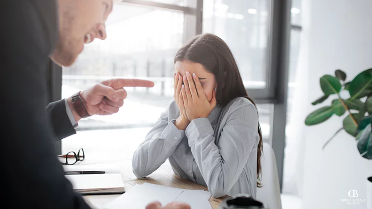 A imagem mostra uma funcionária angustiada sendo confrontada agressivamente por um colega, exemplificando assédio no ambiente de trabalho. Esse comportamento prejudica a saúde mental e o clima organizacional. Empresas devem adotar políticas claras para garantir um ambiente de respeito e dignidade.